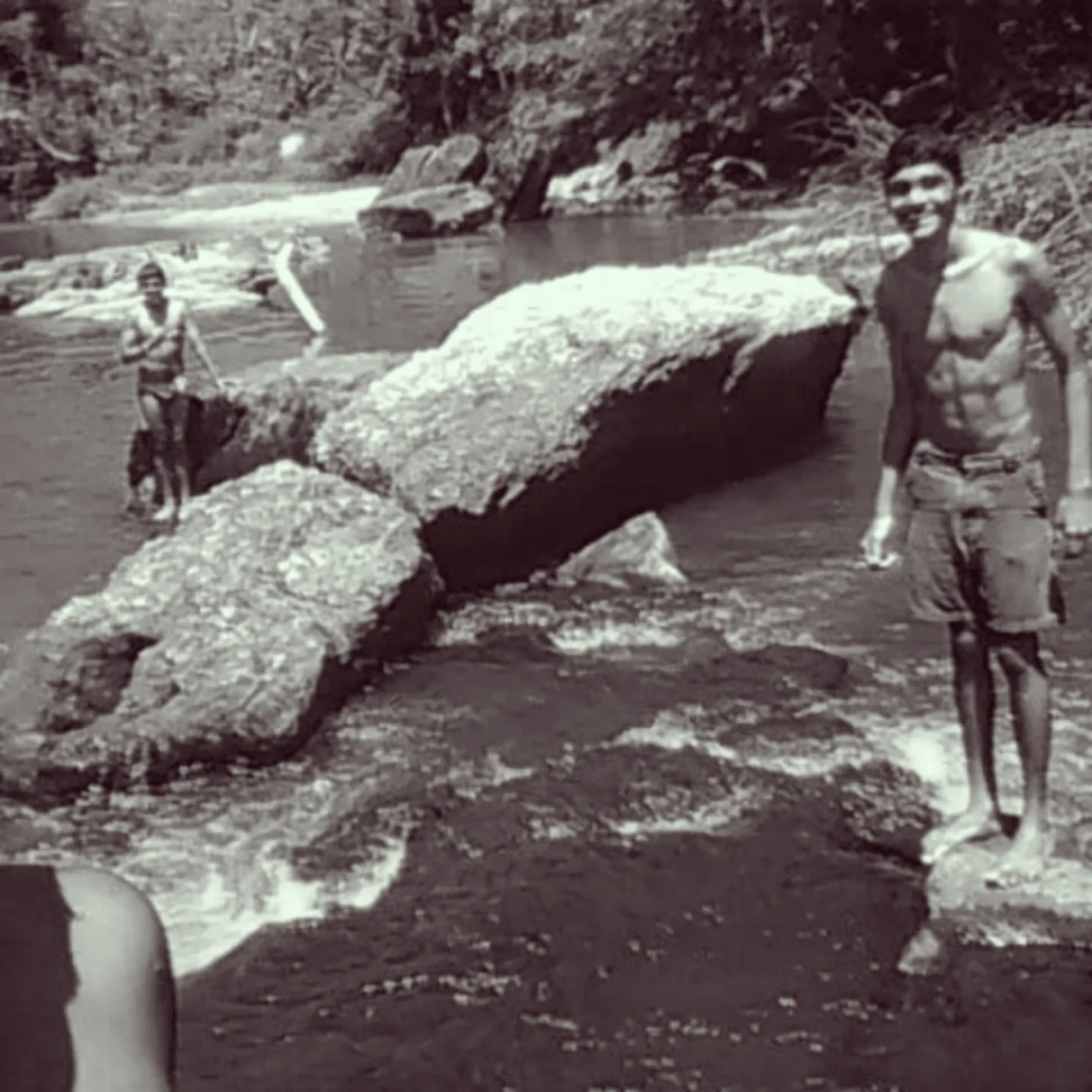 Black and white photo of Chatura standing on rocks in a river, 2018